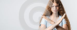 Image of serious blonde girl making X sign with crossed hands. Studio shot, white background. Copy space