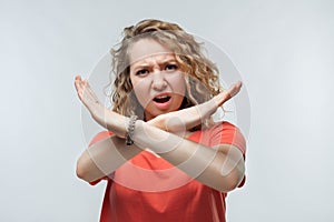 Image of serious blonde girl making X sign with crossed hands. Studio shot, white background. Human emotions concept