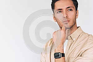 Image of serious thoughtful young man wearing casual formal outfit and smartwatch on wirst, looks away, isolated on white studio