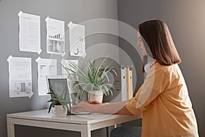 Image of serious woman freelancer wearing yellow shirt having brown hair typing on notebook in office, having concentrated facile photo