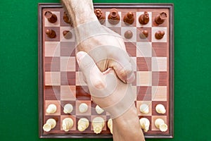 Image of shaking male hands over chess on a green background