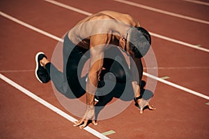 Image of shirtless athlete man preparing for running on racetrack at stadium. Fit male runner sprinting during training session