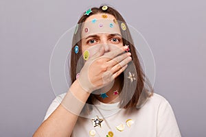 Image of shocked scared woman covered with funny stickers posing isolated over gray background, sees something frighten, covering