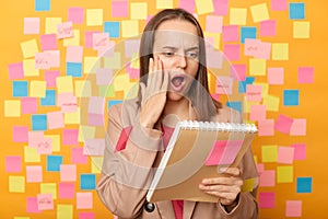 Image of shocked surprised woman wearing beige jacket, holding organizer, reading astonished information, screaming, posing over