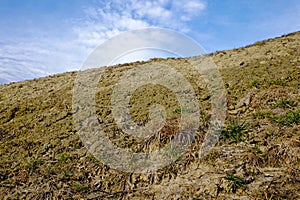 The image showcases a steep hillside with patches of dry grass, set against a blue sky