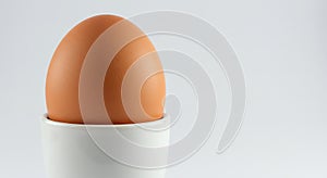 a single brown egg in a white egg cup on a white background - generated using ai