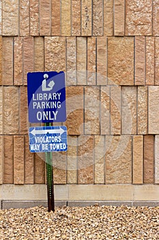 View of a library parking sign in front of an modern limestone wall with rough texture bricks