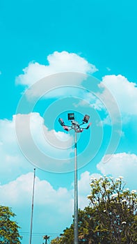 The image shows a street light against a blue sky with clouds in the background. There is also a tree .