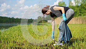 Image of side of woman in rubber gloves picking up garbage in bag on banks of river