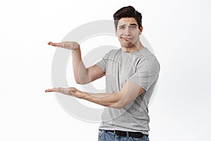 Image of skeptical brunette guy holding empty copy space between hands, showing hand box gesture as if display product