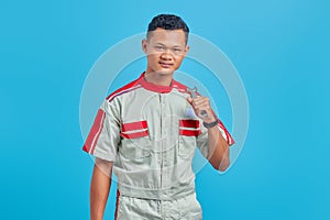 Image of smiling Asian handsome man wearing mechanical uniform holding wrench isolated on blue background