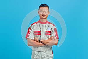 Image of smiling handsome man wearing mechanical uniform looking at camera and crossing hands on blue background