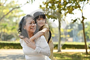 Image of smiling idle age grandmother giving piggyback ride to cute little granddaughter during walking on in the park