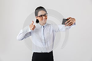 Image of smiling office woman wearing eyeglasses taking selfie photo on cell phone, isolated over white background