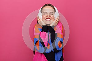 Image of smiling satisfied delighted Caucasian woman wearing warm sweater and fur earmuffs standing isolated over pink background