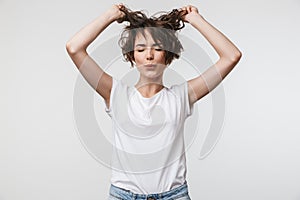 Image of smiling woman in basic t-shirt touching her hair and looking at camera