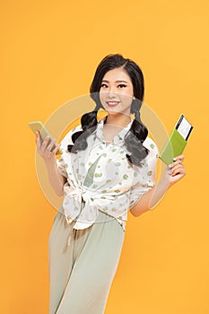 Image of smiling woman holding passport with ticket and mobile phone isolated over yellow background