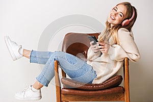 Image of smiling woman using headphones and cellphone while sitting