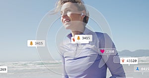 Image of social media data processing over caucasian woman with smartphone on beach