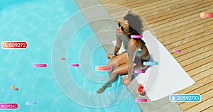 Image of social media notifications over biracial woman sitting by sunny pool