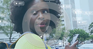 Image of social media notifications over happy african american woman using smartphone in street