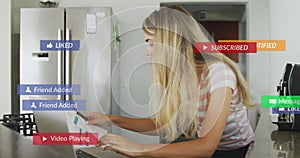 Image of social media notifications over woman working on laptop in kitchen