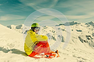 Image of sportive man wearing helmet wearing yellow jacket sitting on snowy slope