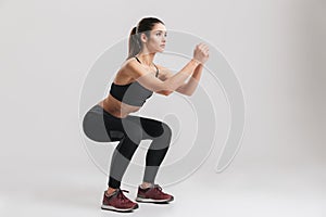 Image of sporty athletic woman in sneakers and tracksuit squatting doing sit-ups in gym, isolated over gray background