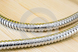 Image of stainless steel shower hose on wood and yellow background