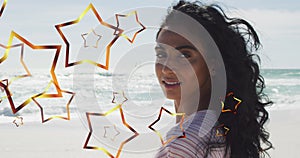 Image of stars over biracial woman at beach