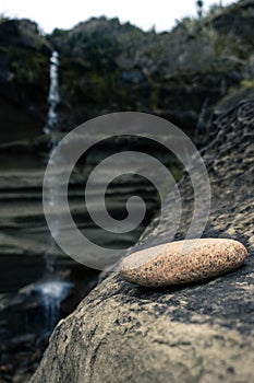 Image of a stone resting on the hillside with the waterfall in the background taken on a cloudy day at Truman Track, New Zealand