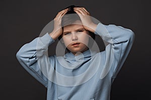Image of stressed boy 10-12 years old grabbing his head. Emotional helplessness. Studio shot, gray background