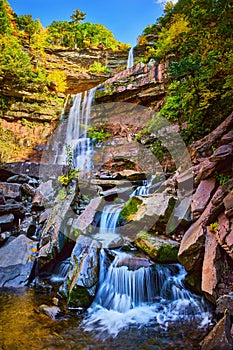 Stunning terraced waterfalls small and large from below over mossy rocks surrounded by New York fall foliage