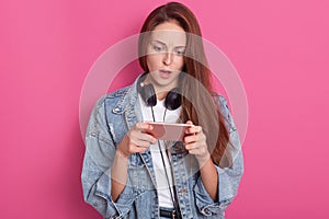 Image of stupefied woman staring at smart phone`s screen with open mouth, watching horrible video in internet, wearing fashionabl photo