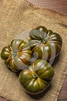 Image of stupendous ripe tomatoes of the sweet mamarlade variety on brown burlap cloth and everything else on a wooden table