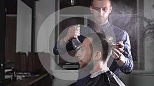 Image of stylish male barber spraying water on hair of client and brushing it to make stylish haircut. Young hairdresser