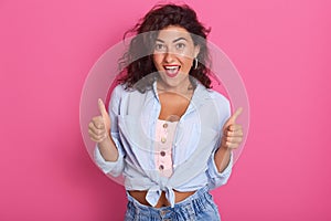 Image of success woman showing thumbs up, excited beautiful lady posing isolated over pink studio background, Caucasian model