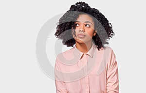 Image of thoughtful African American woman has thinking expression, looking up to the blank copy space. Doubtful dark skinned