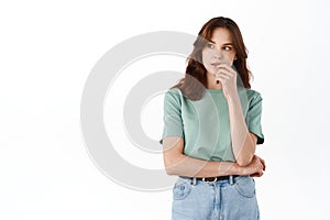 Image of thoughtful young woman touching lips and thinking, looking aside at something interesting, staring curious at