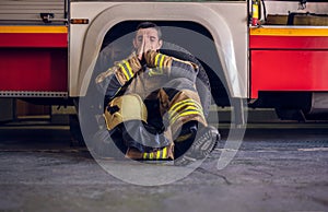 Image of tired fireman sitting on floor near red fire truck