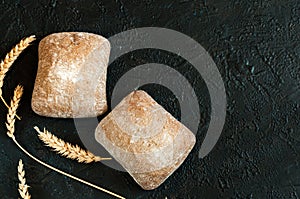 Image of two ciabatta loaves on a black background with ears of rye, top view in natural light