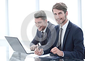 Image of two young businessmen using laptop at meeting