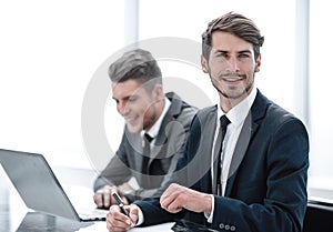 Image of two young businessmen using laptop at meeting