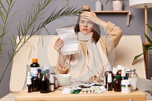 Image of unhealthy ill Caucasian woman reading instructions before taking medication, suffering terrible headache, touched her