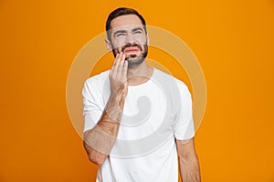 Image of unshaved man 30s in t-shirt touching his cheek and suffering from toothache while,  over yellow background