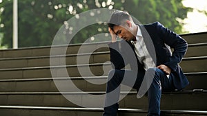 Image of upset man employee sitting on stairs outside office building, financial crisis, unemployed concept