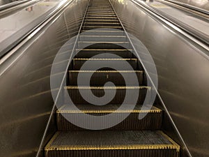 Image of an upward moving silver escalator with yellow safety markings, taken in a public space such as a subway station photo