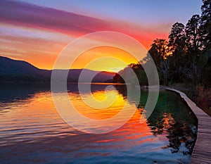 An image of a vibrant sunset over a serene lake, with colorful reflections shimmering