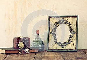 Image of victorian vintage antique classical frame, jewelry and perfume bottles on wooden table. filtered image