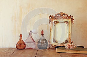 Image of victorian vintage antique classical frame and perfume bottles on wooden table. filtered image